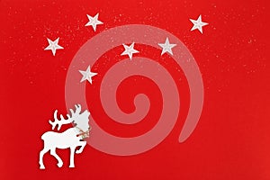Christmas greeting card with white deer in fir tree forest on red background. Star on sky. Winter Holiday concept