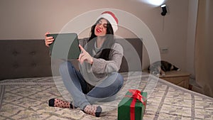 Christmas greetings online. a woman in a gray sweater and a red santa hat uses a laptop to make video calls to friends