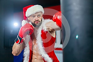 Christmas. A handsome muscular man in a Santa Claus suit with Boxing gloves works out punches on a Boxing bag.