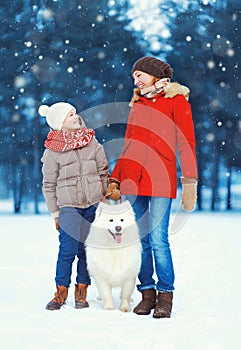 Christmas happy family, mother and son child walking with white Samoyed dog on snow in winter day