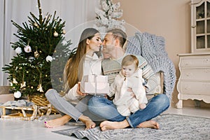 Christmas happy family. Portrait of a father, mother and daughter sitting at home near the Christmas tree. Parents kiss