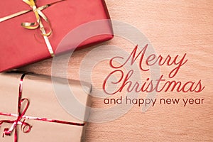 Christmas and happy new year greeting card of two wrapped gifts on wood background with lettering on red