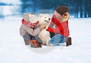 Christmas happy smiling family, mother and son child walking with white Samoyed dog on snow in winter da