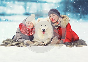 Christmas happy smiling family, mother and son child walking with white Samoyed dog in winter day, lying on snow