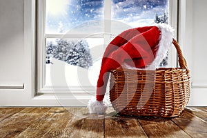 A christmas hat in a basket and snowy winter background outside the window and space for products and decorations.