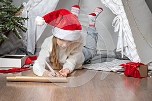 Christmas helper child writing letter to Santa Claus in red hat. smiling girl making wish list or letter to santa at