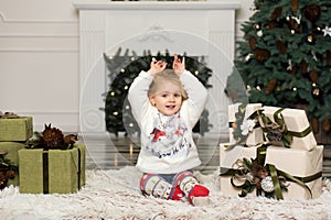 Christmas is here. Little girl plays with pine cones decorations to the Christmas tree. Boxes with gifts are standing on the floor