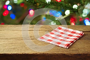 Christmas holiday background with empty wooden table with red checked tablecloth over Christmas tree bokeh. Product montage