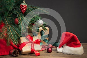 Christmas holiday background. Gifts with a red ribbon, Santa`s hat and decor under a Christmas tree on a wooden board.