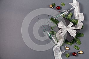 Black handmade gift boxes decorated with silver ribbon, tree branches, two glasses champagne confetti on gray background.