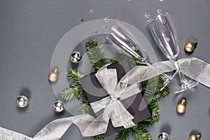 Black handmade gift boxes decorated with silver ribbon, tree branches, two glasses champagne confetti on gray background.