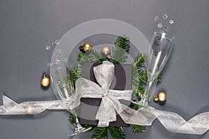 Black handmade gift boxes decorated with silver ribbon, tree branches, two glasses champagne confetti on gray background.