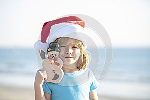 Christmas holiday concept. Child Santa with toy smowman on the sunset sea. Santa and snowman on summer beach, concept