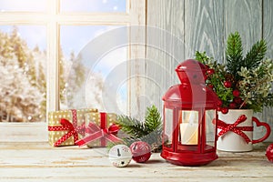 Christmas holiday concept with lantern and gift box on wooden table over window winter landscape background. New Year greeting