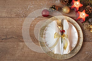 Christmas holiday dinner place setting - plates, napkin, cutlery, gold bauble decorations over oak table background. Fork and