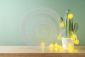 Christmas holiday greeting card with cactus as alternative Christmas tree and  lights garland on wooden shelf over green