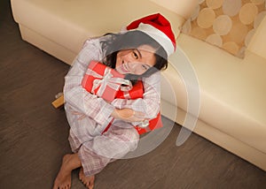 Christmas holiday lifestyle portrait at home of young beautiful and happy Asian American woman in pajamas and Santa hat  holding