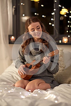 Happy young woman playing guitar in bed at home