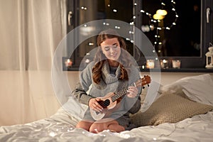 Happy young woman playing guitar in bed at home