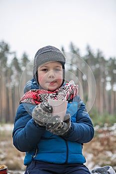 Christmas holidays, boy  drinking  hot New Year beverage. Happy family on a walk outdoors in sunny winter forest