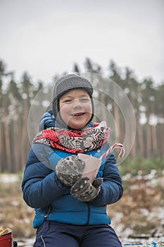 Christmas holidays, boy  drinking  hot New Year beverage. Happy family on a walk outdoors in sunny winter forest