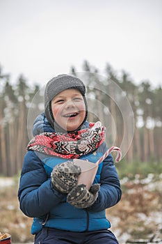 Christmas holidays, boy  drinking  hot New Year beverage. Happy family on a walk outdoors in sunny winter forest