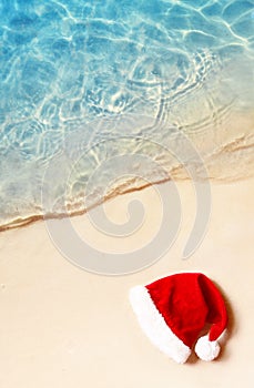 Christmas holidays concept. Top view of santa claus hat on summer sand beach