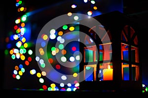 Christmas holidays festive lights inside home in dark room with foreground lantern with candle and background blurred bokeh