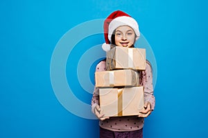 Smiling teenage girl in santa helper hat holding gift box over lights on blue background