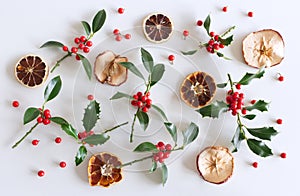 Christmas holly with red berries, dried apple slices and oranges. Traditional festive decoration. Holly branch with red berries on