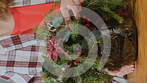 Christmas home decor. Woman making Christmas flower arrangement. Vertical video.