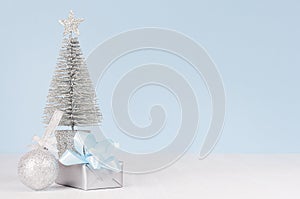 Christmas home decoration - silver fir with festive gift box with blue silk bow and sparkles ball on white wood board and pastel.