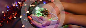 Christmas homemade DIY craft toy for the Christmas tree a cone with glitters in kids hands and New Year lights glowing garlands. b