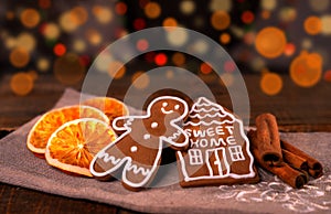 Christmas homemade gingerbread cookies on wooden table, slices of dry orange and colored lights on background