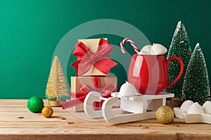 Christmas hot chocolate cup with marshmallow and Christmas decorations on wooden table over green background