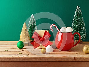 Christmas hot chocolate cup with marshmallow, gift box and decorations on wooden table over green background. Festive greeting