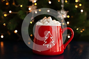 Christmas hot chocolate with marshmallows in a red mug with a garland on the background.Christmas and new year