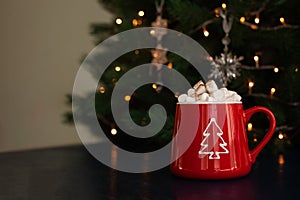 Christmas hot chocolate with marshmallows in a red mug with a garland on the background.Christmas and new year