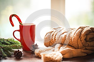 Christmas Hot Coffee in red cup on wooden table on a frosty winter day window background with knitted scarf, candy and christmas