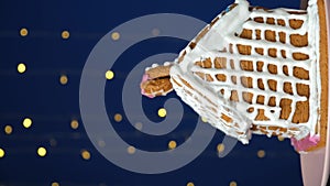 Christmas house made of gingerbread cookies decorated with sugar icing on blue background with bokeh garland