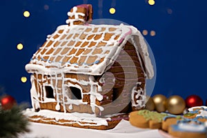 Christmas house made of gingerbread cookies decorated with sugar icing on blue background with bokeh garland