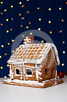 Christmas house made of gingerbread cookies decorated with sugar icing on blue background with bokeh garland