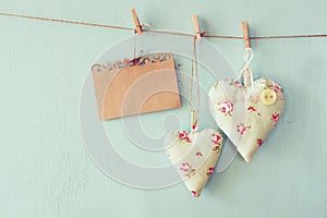 Christmas image of fabric hearts and empty card for adding text hanging on rope in front of blue wooden background. retro filtered