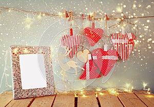 Christmas image of fabric red hearts and blank frame, garland lights, hanging on rope in front of blue wooden background