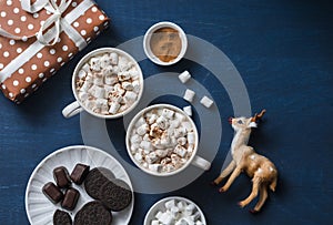 Christmas inspiration table - hot chocolate with marshmallows, cookies, gift box, christmas ornament reindeer on a blue background