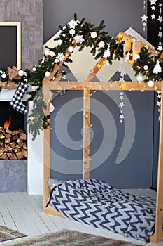 Christmas interior of children`s bedroom with wooden bed in shape of house. New Year decor and New Year fir-tree garland in a chil photo