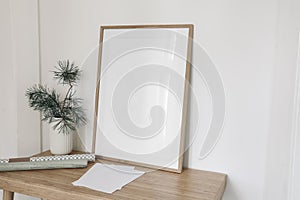 Christmas interior still life. Blank vertical wooden picture frame mockup on wooden table, desk. Pine tree branches in