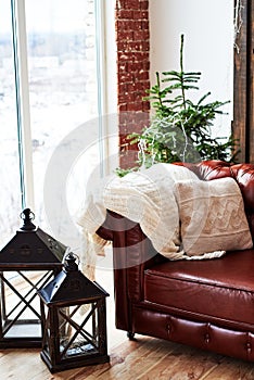 Christmas interior with vintage brown leather sofa, fir tree and lanterns in loft room with panoramic window, copy space.