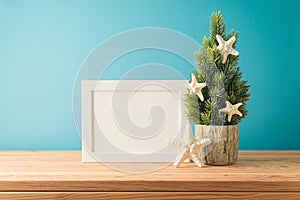 Christmas in July concept with Christmas tree, frame mock up and starfish on wooden table over blue background