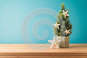Christmas in July concept with Christmas tree and starfish on wooden table over blue background